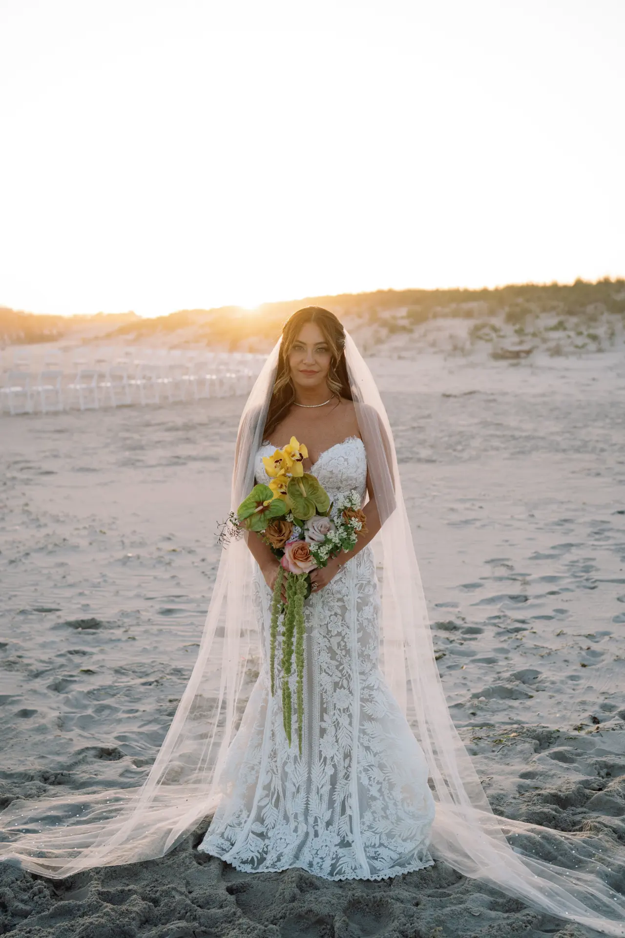 Bride in a lace gown and cathedral veil at a beach ceremony at sunset