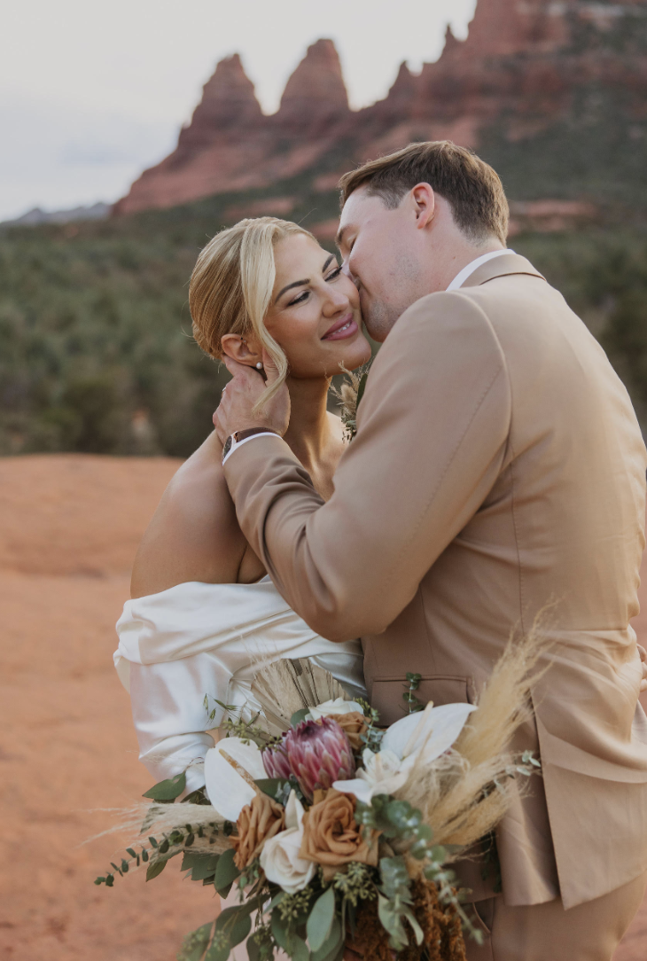 Groom kissing his bride on the cheek in a desert landscape