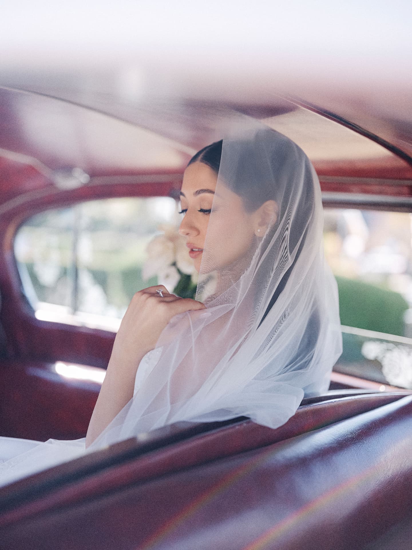 Bride in a cathedral veil looking out of a vintage car window